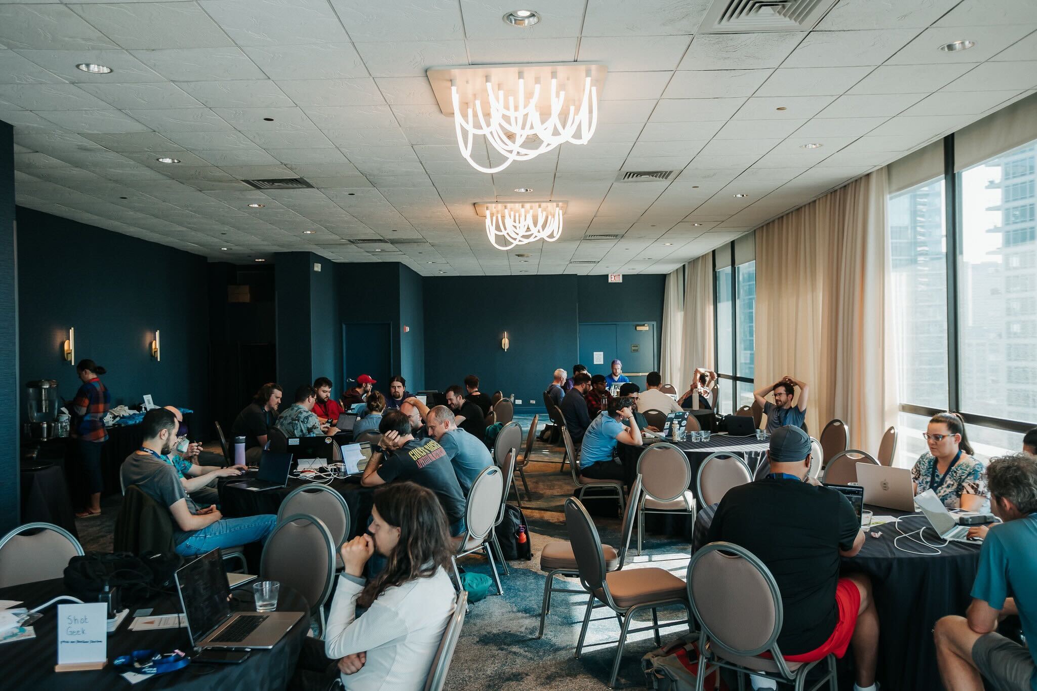 The sprints room at DjangoCon US, filled with attendees working together at round tables.